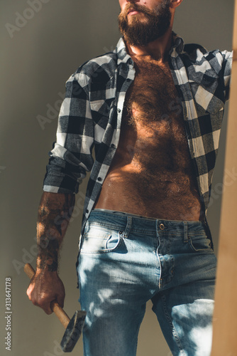 A young brutal man with a beard holds a hammer and a wooden stepladder.