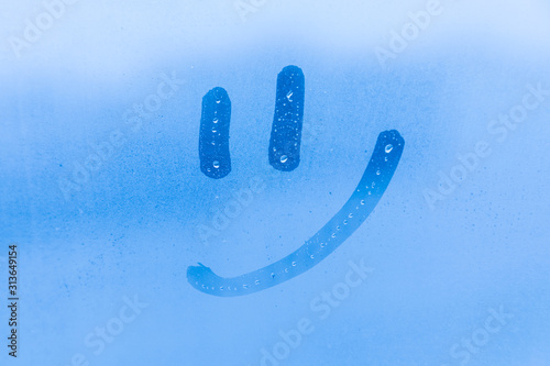 The picture or figure of the smiling face on the blue evening or morning window glass with drops 