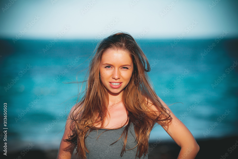 portrait face of a beautiful young girl sunbathing in the sun on the beach paradise looks with one eye wink and squinting at a very bright sunny warm day and smiling