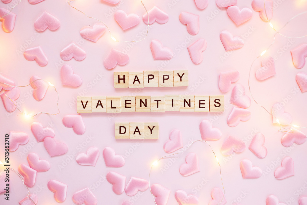 Confetti heart and lights on a pink pastel background with wooden letters. Valentine's day greeting card concept. Top view, flat lay.
