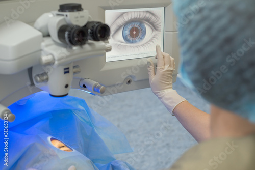 Doctor ophthalmologist, pressing the button on the control display to start a modern laser for the correction of visual impairment. Laser eye microsurgery.