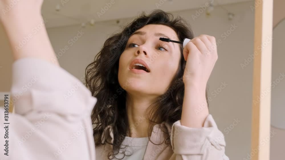 Young female holding mascara apply on eyeleashes prepare getting ready in the morning. She looks at herself in the mirror and smiles. Woman doing makeup. Get ready for a date. Young female holding mascara apply on eyeleashes prepare getting ready in the morning. She looks at herself in the mirror and smiles. Woman doing makeup. Get ready for a date.