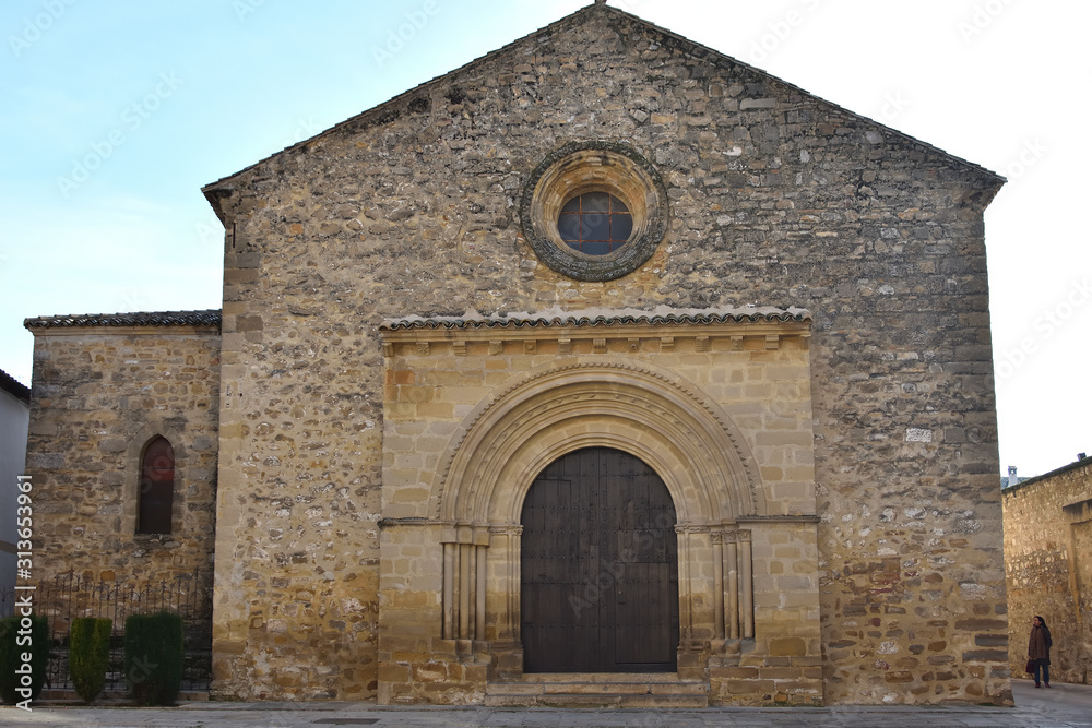 Front view of the Romanesque church of Santa Cruz in Baeza with a woman coming out of a side alley