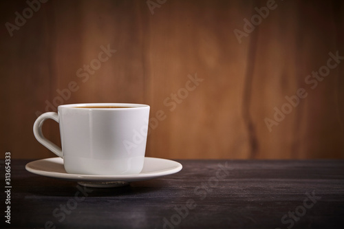 White cup of coffee on brown wooden background with copy space. Close up.