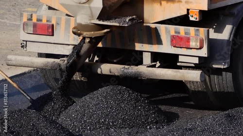 Truck dumping hot asphalt on the road. Large industrial machine pour asphaltic concrete on the street. The dump truck unloads rubble for laying roads. Hauling & dumping asphalt into paver site