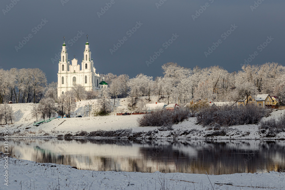Fototapeta premium St. Sophia Cathedral across the river illuminated by the sun rays through the dark sky overcast. Polotsk, Belarus.