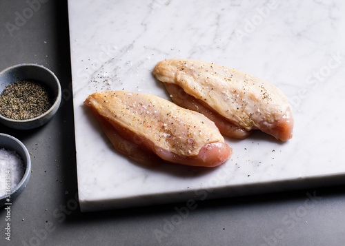 Close up of chicken breasts with salt and pepper on marble board photo