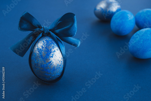 Blue easter egg with ribbon on dark background. Easter stylish minimal composition. Copy space, close up