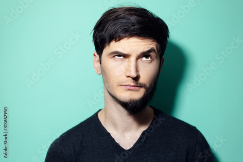 Studio portrait of young man with half shaved face looking up on background of aqua menthe color. © Lalandrew
