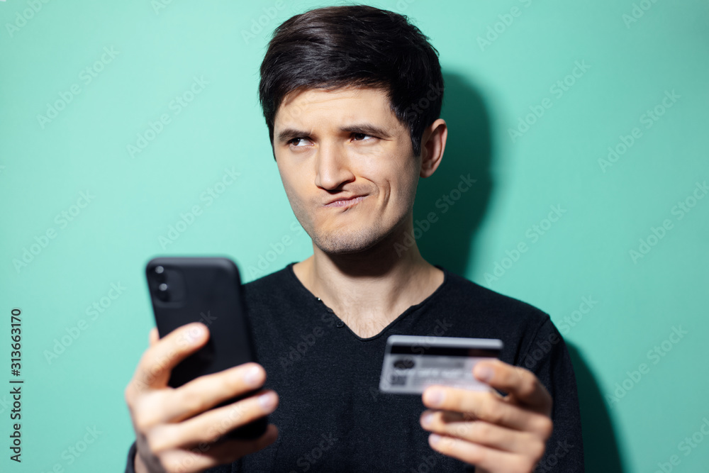 Studio portrait of young surprised man with smartphone and credit card in hand on background of aqua menthe color. Studio portrait of young surprised man with smartphone and credit card in hand on background of aqua menthe color.