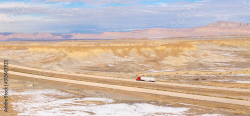 DRONE: Red semi-trailer truck hauls a heavy container across the snowy desert.