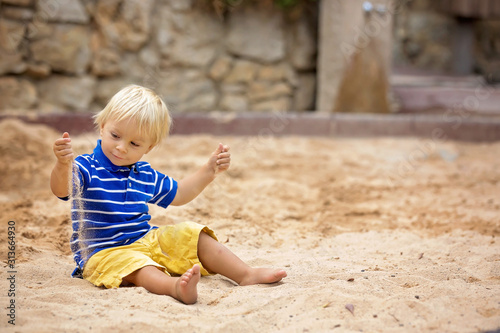 Fototapeta Little toddler boy, playing with sand in sandpit at the playground