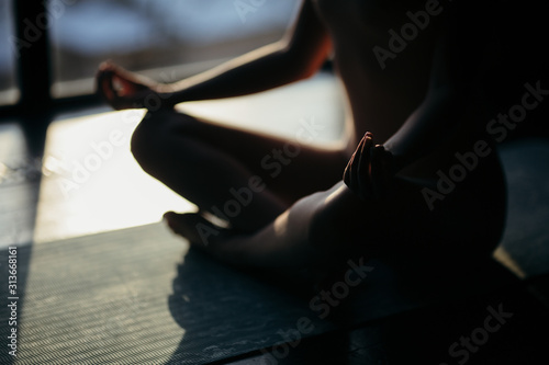 Back view of healthy young woman practicing yoga and sitting in padmasana at training hall or home