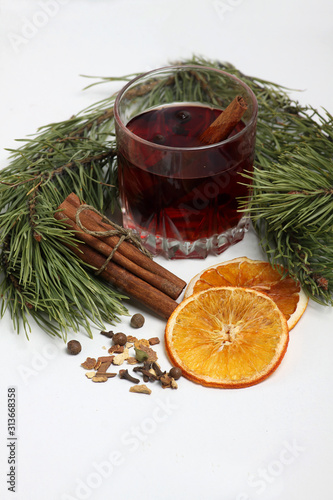 glass of mulled wine, cinnamon sticks, spice and orange chips with fir bough on white background close up. Vertical image