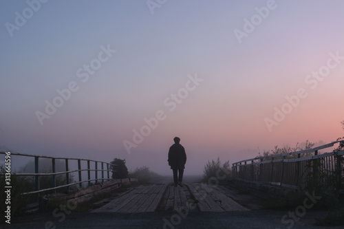 a man walks on a wooden bridge in the fog at morning dawn
