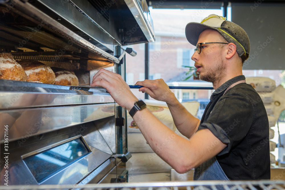 Professional baker stands in front of large oven full of bread loaves Professional baker stands in front of large oven full of bread loaves