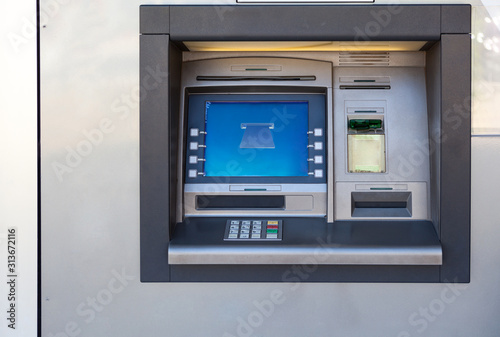 Silver atm machine with screen and buttons is in building wall, nobody