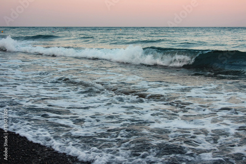 Sea waves crashing at sunset on the shore of the black  volcanic Kamari beach on the island of Santorini
