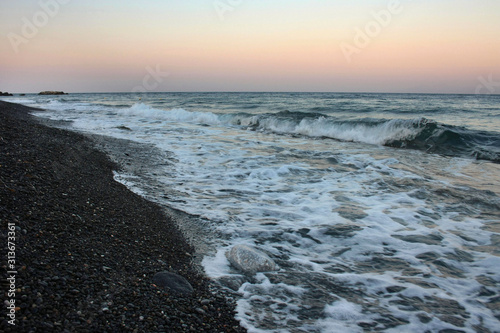 Sea waves crashing at sunset on the shore of the black, volcanic Kamari beach on the island of Santorini