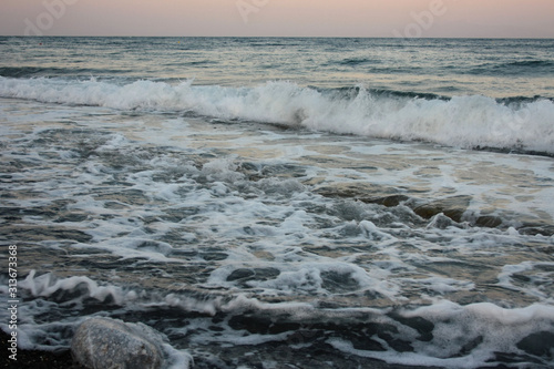 Sea waves crashing at sunset on the shore of the black, volcanic Kamari beach on the island of Santorini
