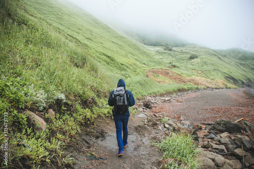 Fotografía male tourist with a backpack goes backwards in the wild at the foot of a mountai