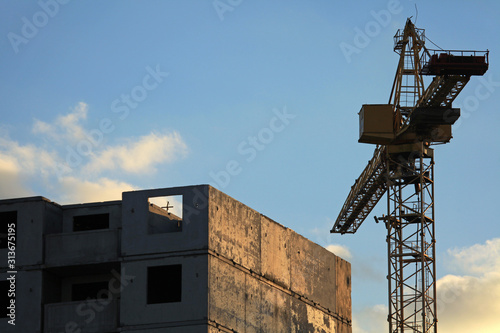 An old construction crane and unfinished panel multifamily house at the frozen and abandoned construction site. Building construction site with crane. The construction of modern apartment buildings