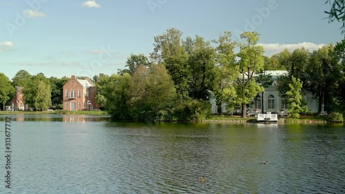 Gimbal shot left to right of Tsarskoe Selo view grot pavillion Catherine Garden surrounded by green trees under cloudy blue sky. A small island with green trees in summer time photo