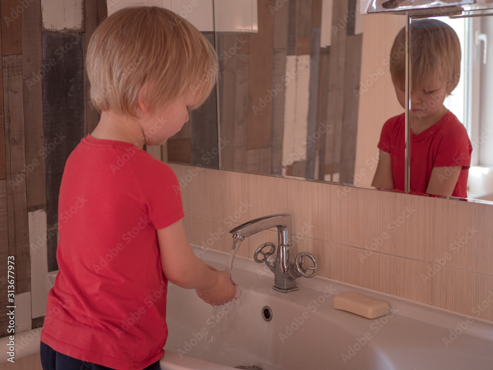 Happy boy washes hands with soap. Child playing with bar of soap and water in sunny bathroom with window. Water activities for children. Hygiene and skin care for children. Bathroom interior Happy boy washes hands with soap. Child playing with bar of soap and water in sunny bathroom with window. Water activities for children. Hygiene and skin care for children. Bathroom interior