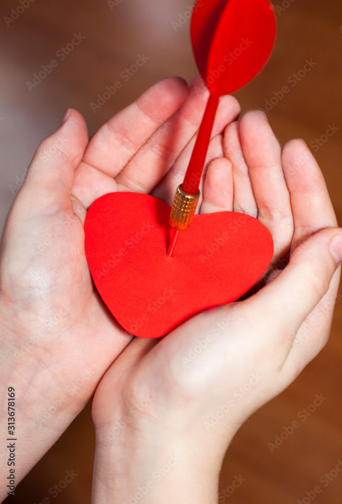 Red heart pierced by an arrow or dart in the palms. The concept of unsuccessful or broken love. Valentine's Day.