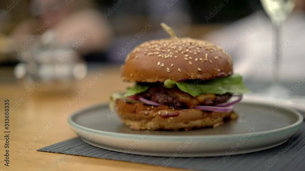 Gimbal pan shot left to right of a fresh burger with meat and vegetables on a plate served at the restaurant. Burger fast food dish on blurred background in the restaurant Gimbal pan shot left to right of a fresh burger with meat and vegetables on a plate served at the restaurant. Burger fast food dish on blurred background in the restaurant