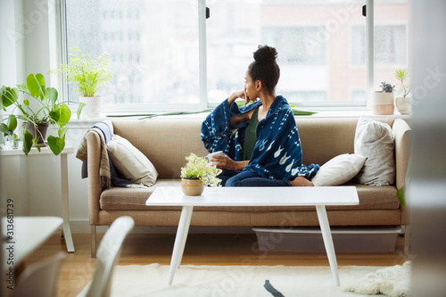 Bild auf Leinwand Thoughtful young woman looking away while having coffee in living room at home