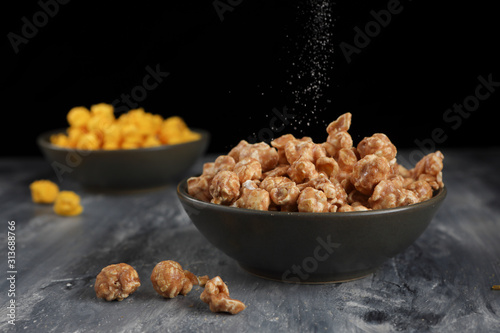 Pouring salt on popcorn in a bowl.