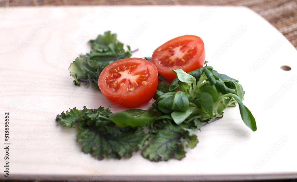 Spinach fresh, other greens and tomato cut into two pieces on wooden board Spinach fresh, other greens and tomato cut into two pieces on wooden board