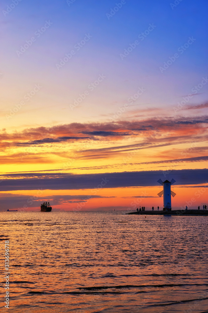 Tourist boat in the Baltic Sea with beautiful sunset over a windmill shaped lighthouse in Swinemünde. Swinoujscie, Poland