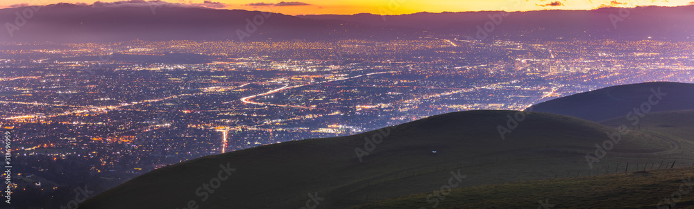 Panoramic night view of San Jose, Silicon Valley; the downtown area buildings visible on the right; green hills partially blocking the view; San Francisco Bay Area, California - obrazy, fototapety, plakaty 