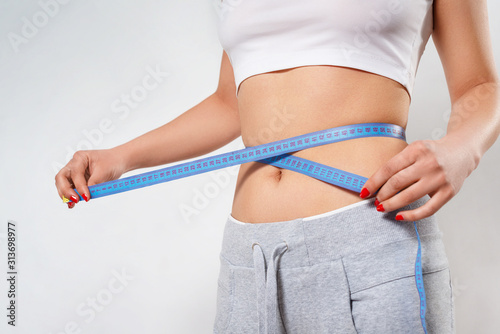 a young slender woman measures her waist with a centimeter tape. on white background