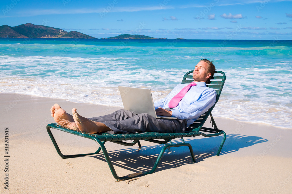 Businessman working on his laptop on a beach chair relaxing on the shore of an empty tropical beach
