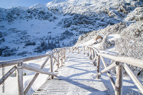 górski krajobraz, oblodzony drewniany most, śnieg i piękne niebieski niebo