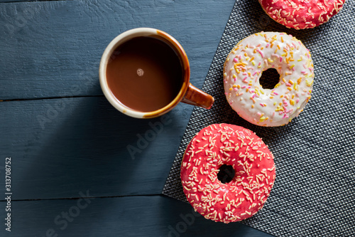 Colorful glazed donuts and chocolate cup on dark wooden background. Top view.