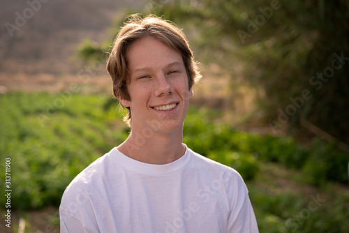 A handsome teenage boy smiles at the camera in the late afternoon sun.