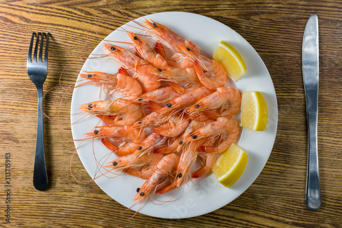 White plate with tasty shrimps with lemon served on old style table with fork and knife. Top view