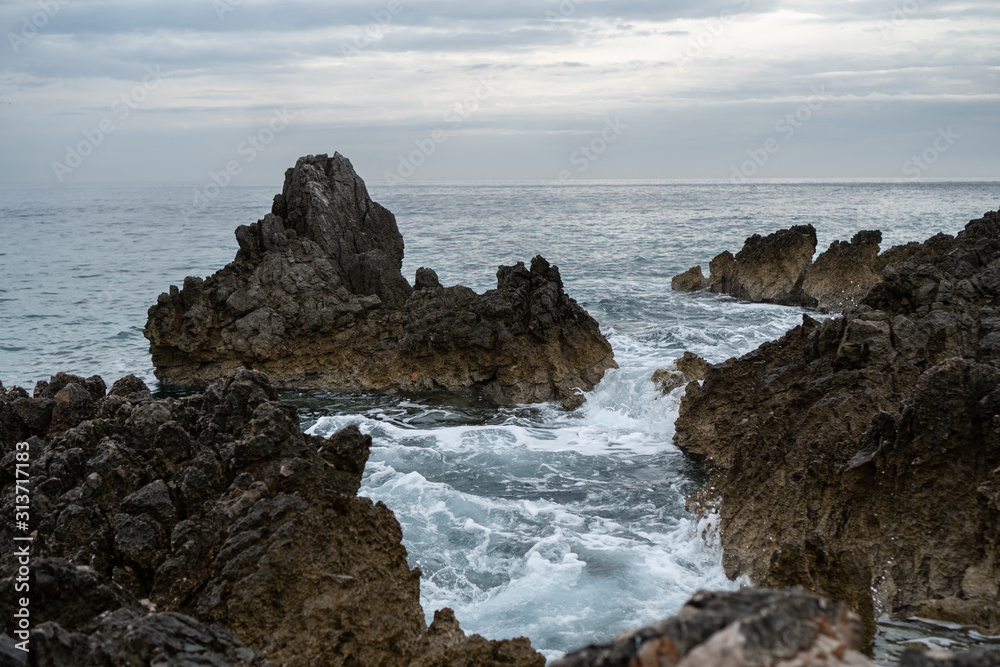 Rock sticking out of the sea in the background of gray sky and horizon