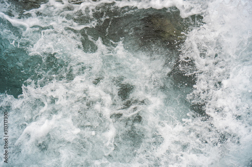 Raging blue water in a backwater with stones and white foam.