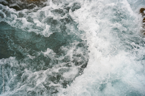Raging blue water in a backwater with stones and white foam.