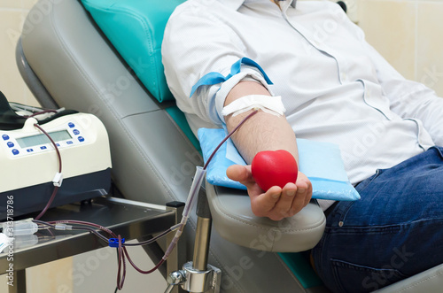 blood donation. man in hemotransfusion center holds rubber red ball in the form of heart. soft focus photo