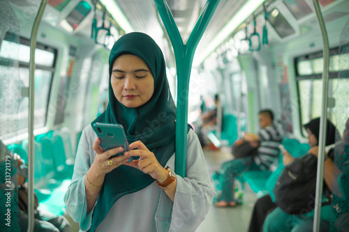 Young Muslim woman traveling inside subway train standing while using phone. Transportation and technology concept. 