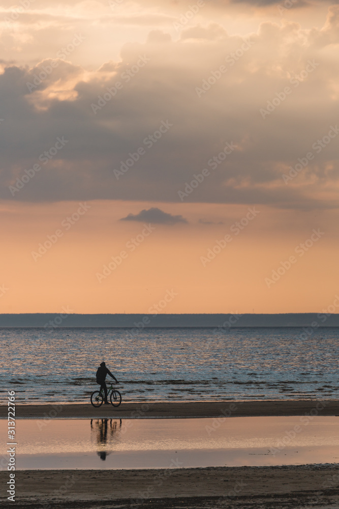A man on a bicycle enjoys of calming scenic landscape above the sea. Gentle tones of the scenery. Bike ride along the Bay. Travel and vacation concept. Inspirational vertical photo. Beauty world.