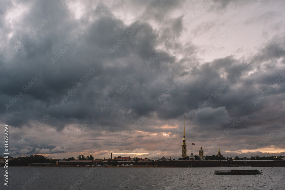 Dramatic sky above Peter and Paul fortress in Saint Petersburg. The boat is floating on the Neva river. Copy space. The most tourist city in Russia. Tourism and vacation concept.