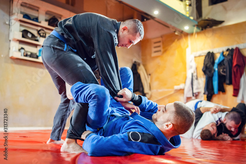 Two brazilian jiu jitsu BJJ athletes training practicing position drilling the technique from the guard sparring wearing blue and black kimono holding sleeve de la riva