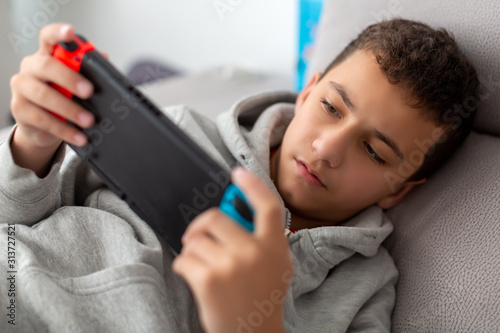 boy plays video games on a portable console while lying on a sofa